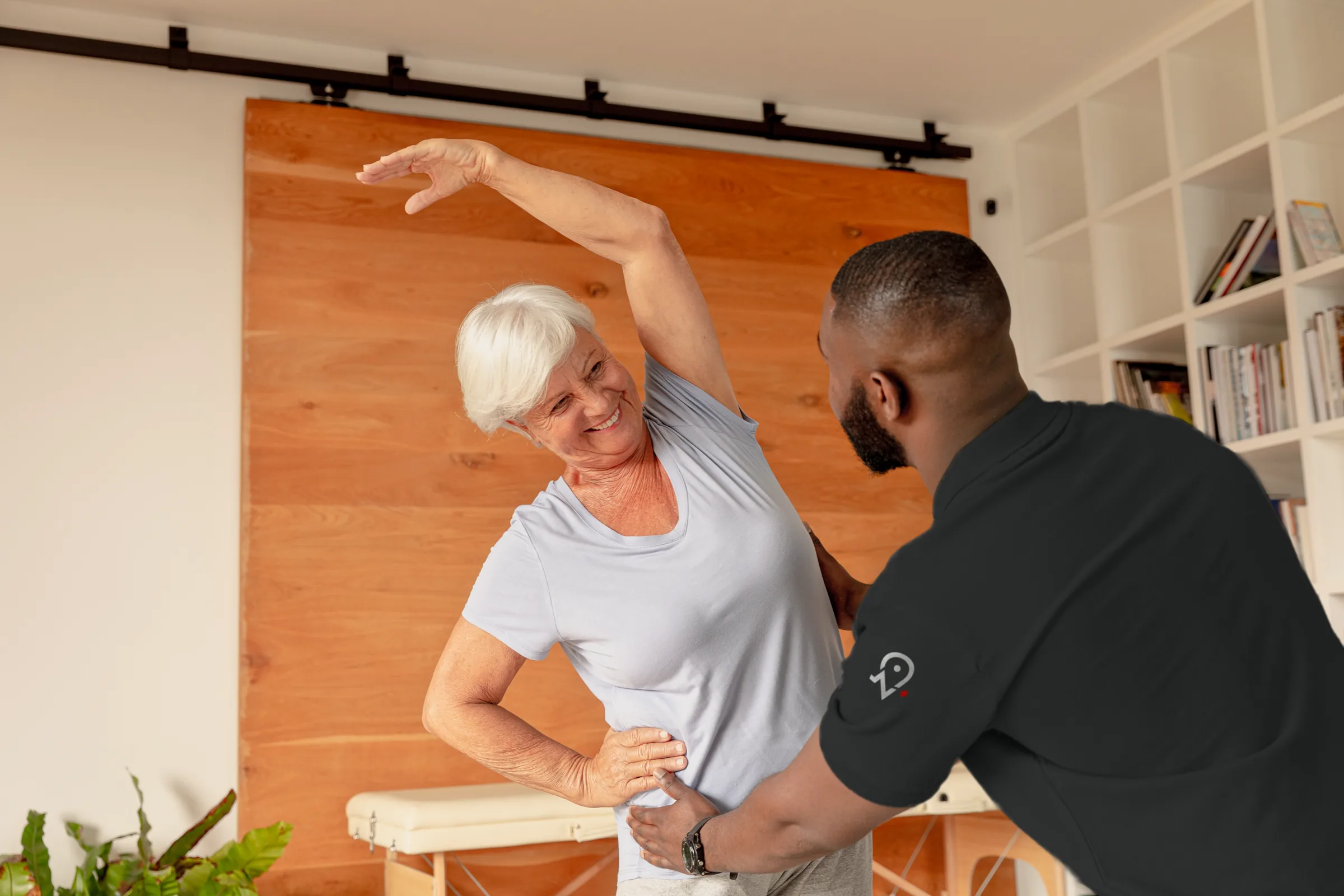 Une senior fait un étirement latéral, accompagnée par son coach.