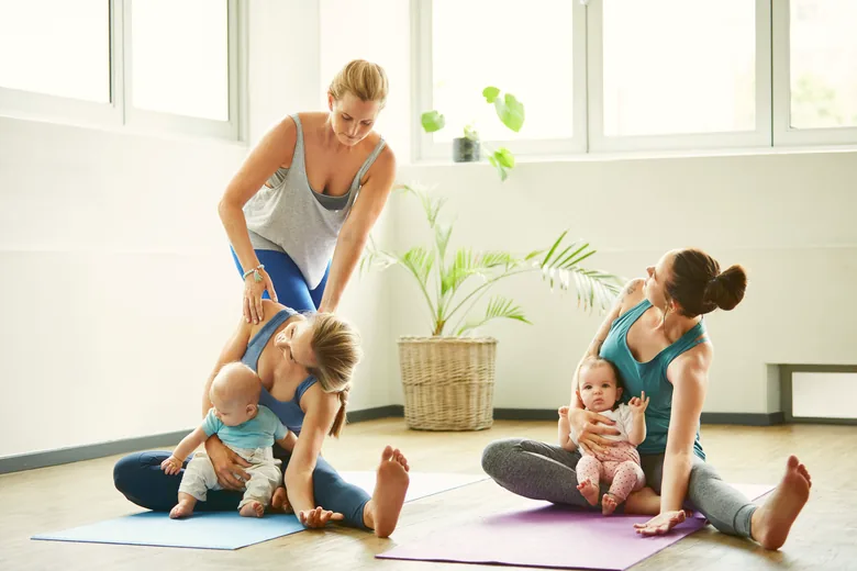 Une coach corrige la posture d'une femme assise avec son bébé, à côté d'une autre mère et du sien.