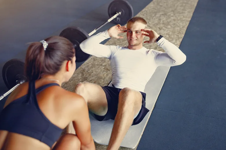Une coach suit un sportif pendant une série d’abdominaux.