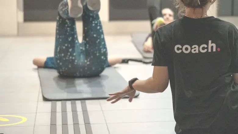 Une coach guide du geste une participante en appui au sol.